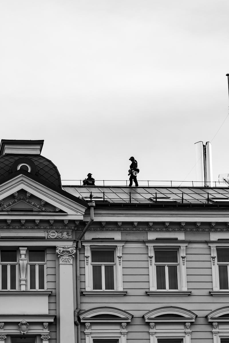 Black and white photo of workers walking on a historic building's rooftop in an urban setting.
