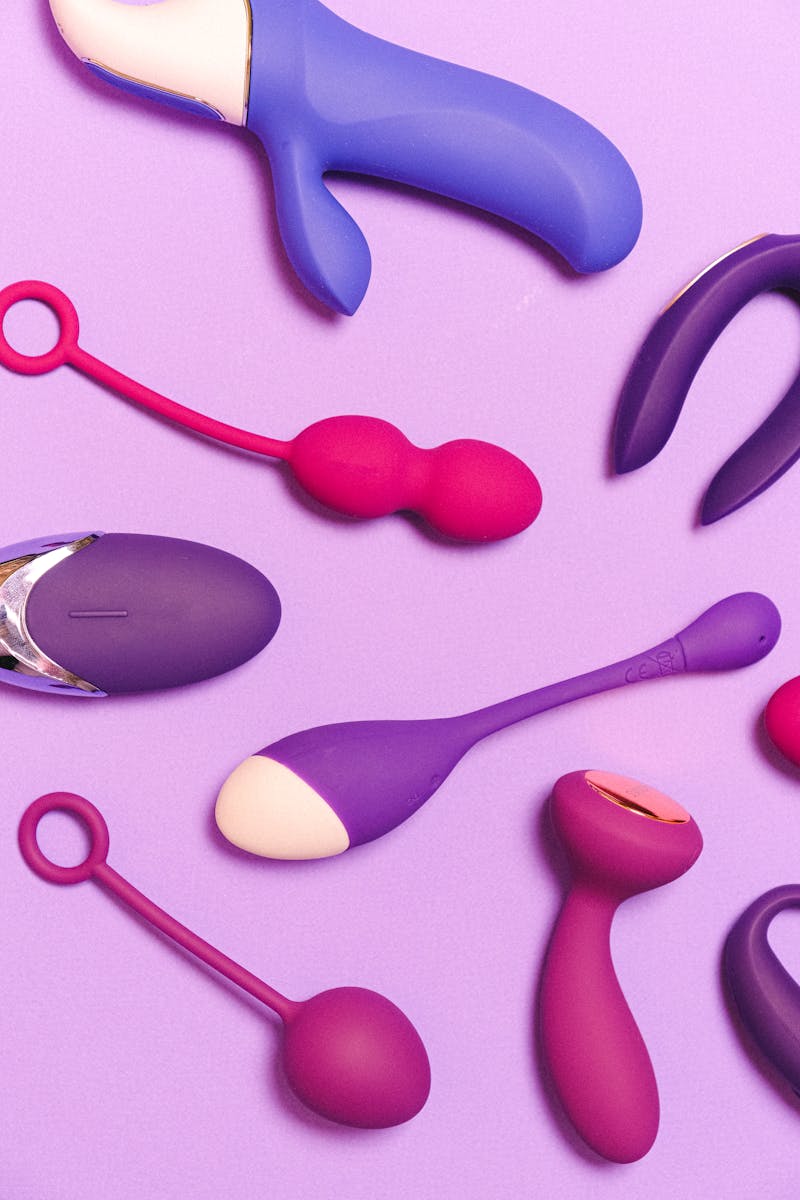 A variety of silicone sex toys arranged aesthetically on a purple surface.